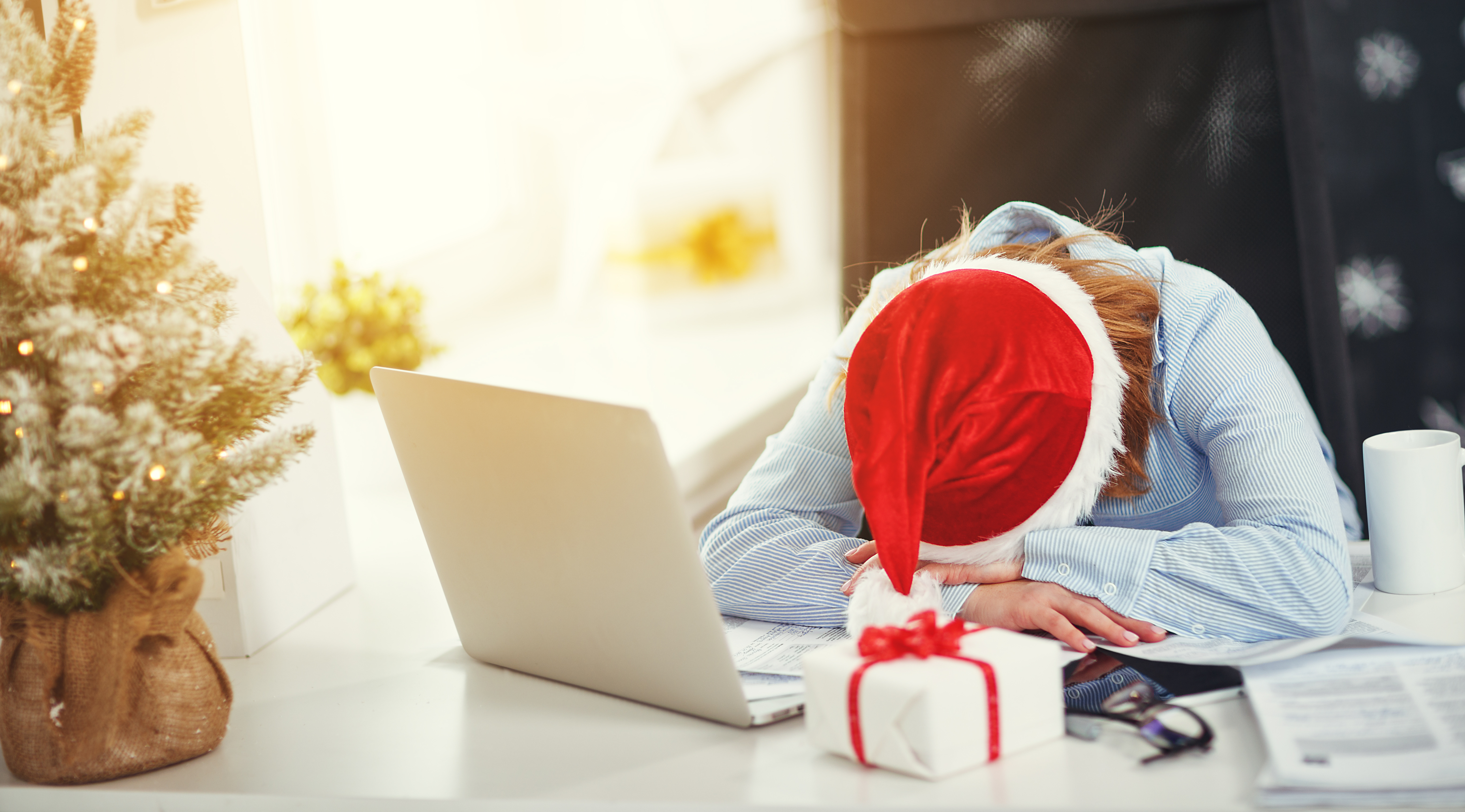 Woman in a Santa hat laying her head on her desk with her computer open.
