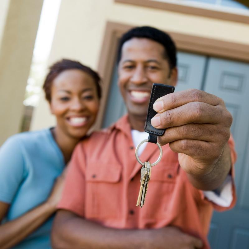 Couple holding up keys in front of their new house.