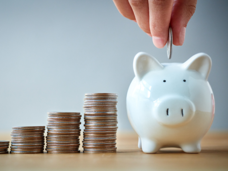 Finance Tips Someone adding change to a piggybank with stacks of quarters sitting next to it.