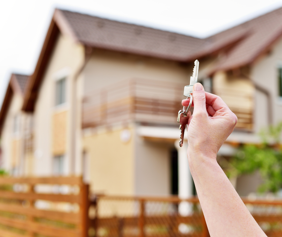 Mortgage Someone holding house keys in front of a new house.