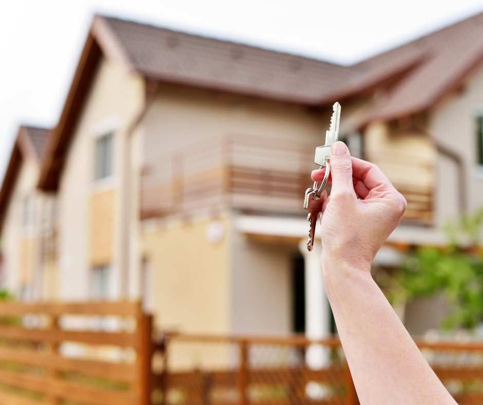 Someone holding house keys in front of a new house.